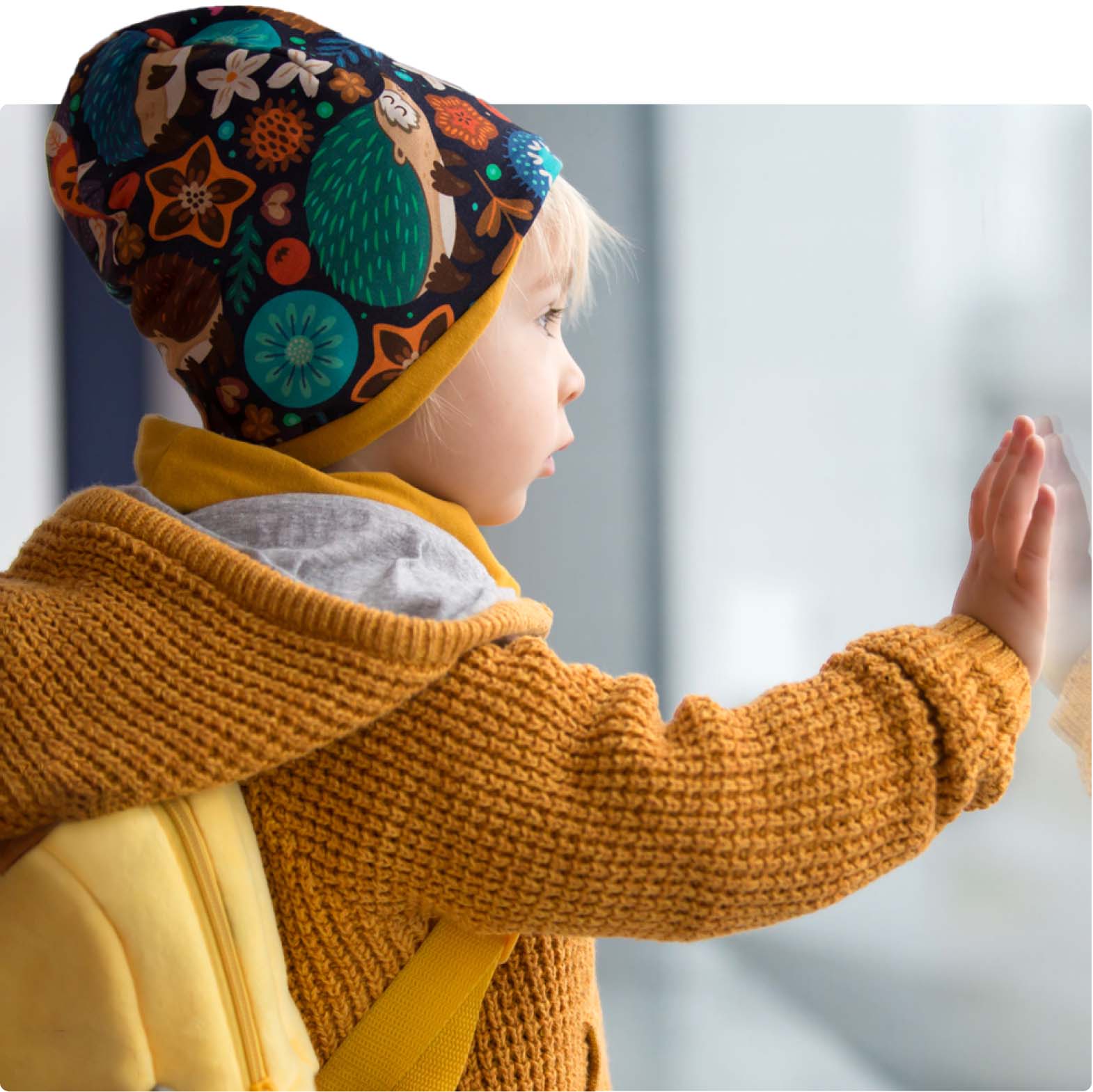 Young boy in yellow jumper pressing his hand to the window