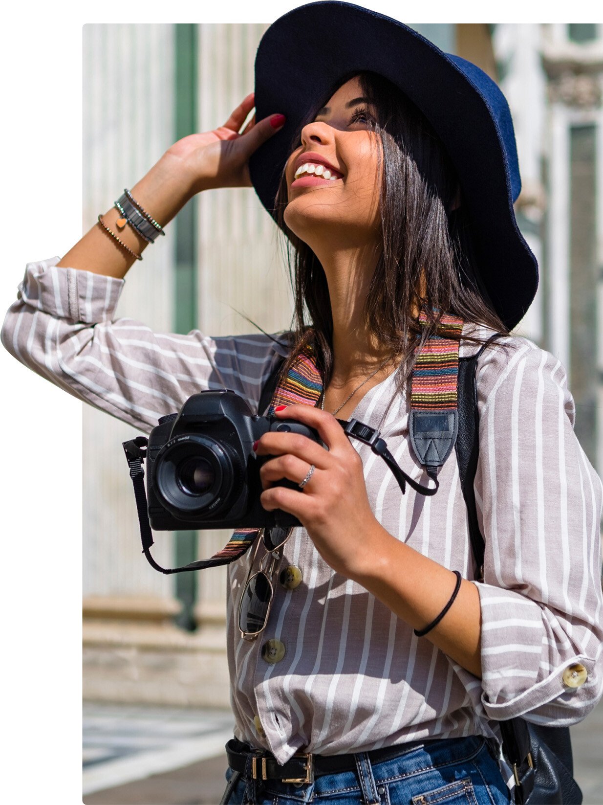 Young woman holding a camera and wearing a hat looking up at an unknown object